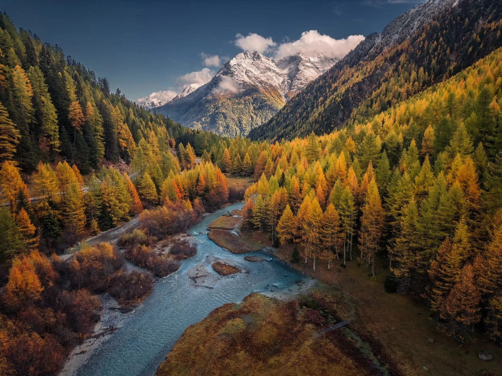 An alpine stream winding through forest beneath a mountain peak